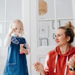 A joyful moment of a mother and daughter playing with bubbles indoors.